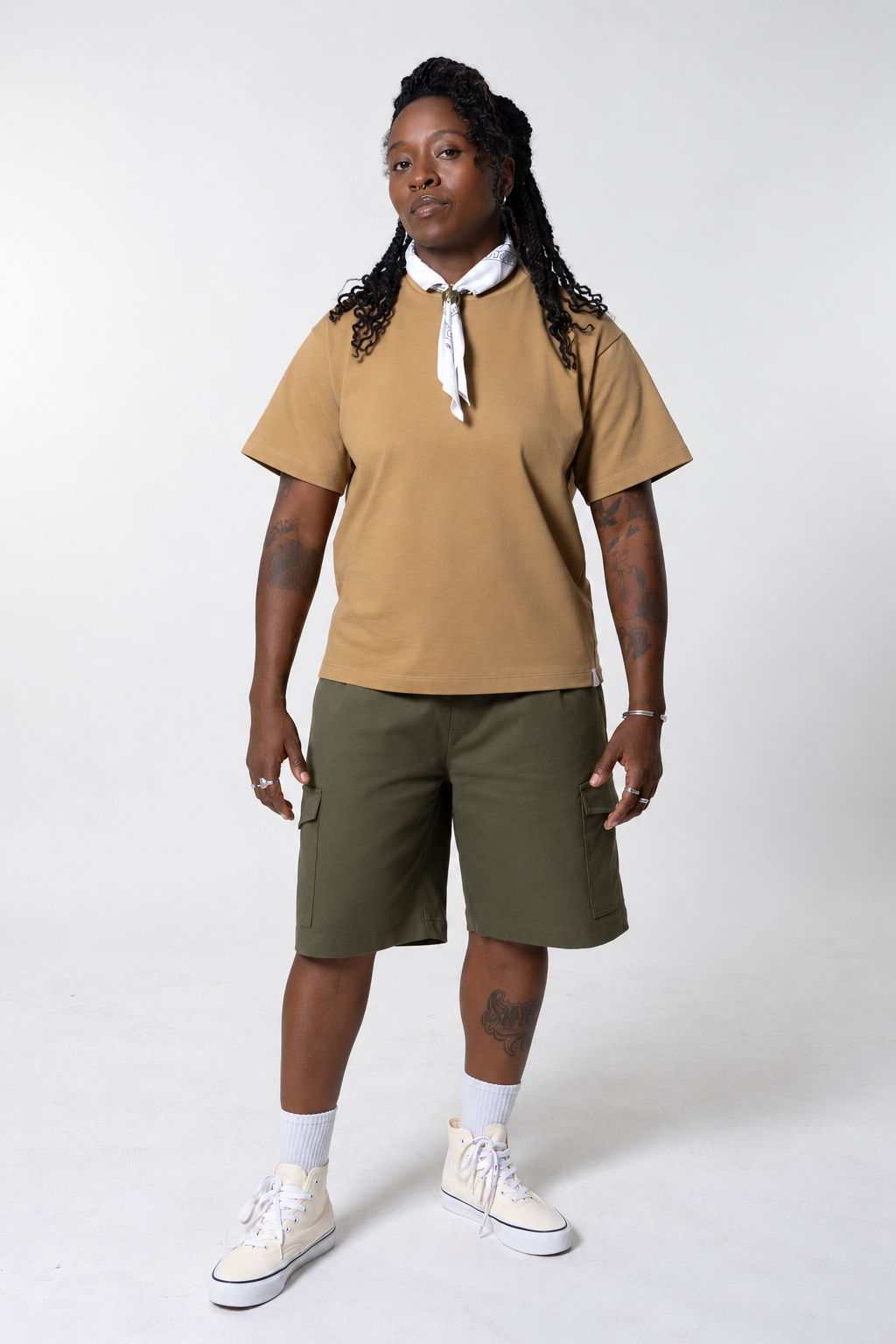 Woman in the Mich boxy tee in dune with a white neck scarf, olive cargo shorts and cream high-top sneakers.