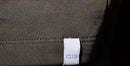 White logo label 'a13' in stitched on gray fabric against jean pant.