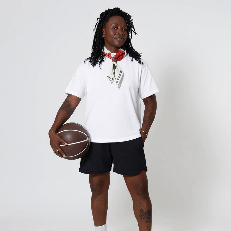 Woman in the white Mich boxy tee and black Andi shorts, red and cream silk scarf at the neck, vintage basketball at her hip.